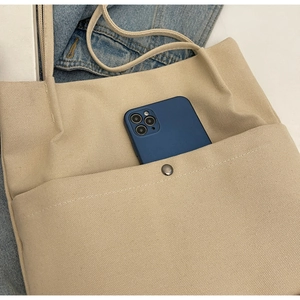Close-up of beige canvas tote bag showing the front pocket with a smartphone inside