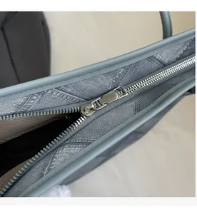 Macro view of a smooth silver metal zipper and brown herringbone lining on a gray tote bag