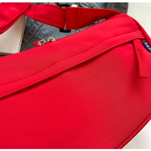 Close-up of red nylon crossbody bag with silver metal zipper and woven brand label