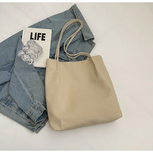 Detail of a minimalist cream canvas tote bag styled with casual denim and lifestyle books