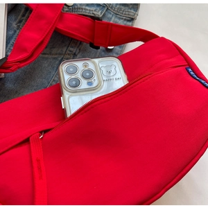 Detail of red nylon crossbody bag with zipper pocket and blue brand logo label