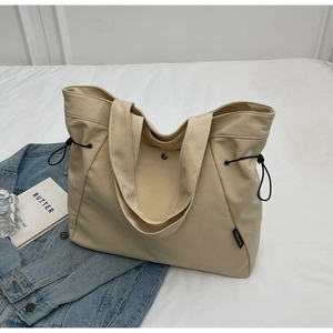 Detailed side view of beige canvas tote bag featuring black drawstring and brand tag