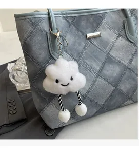 Detail of white plush cloud charm with smiley embroidery on blue denim texture tote bag