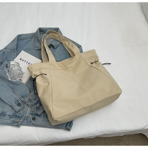 Detail of cream nylon tote bag with side drawstring accents and soft texture