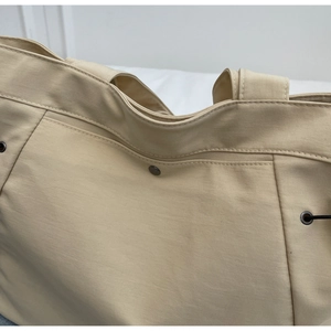 Detail of beige nylon tote bag showing precision stitching and metallic eyelet accents