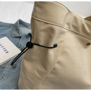 Detail of beige nylon tote bag featuring black drawstring and plastic toggle fastener