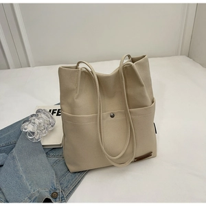 Close-up of beige canvas bucket bag featuring a front pocket and metal snap button