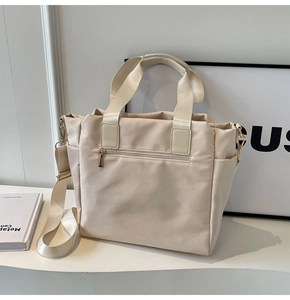 Detail view of beige nylon tote bag showing gold zippers and detachable strap
