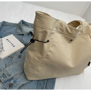 Detail view of large cream nylon tote bag with functional side drawstring and toggle
