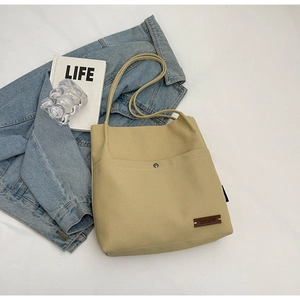 Detail of canvas tote bag featuring leather brand tag and front pocket with metal buckle