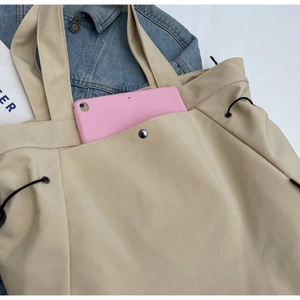 Detail of beige nylon tote bag showing front pocket with snap and interior tablet capacity