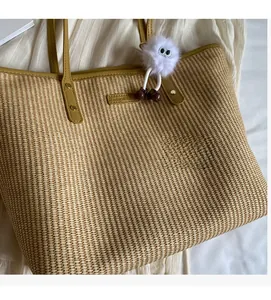 Détail du sac cabas en paille avec lanières en cuir marron et breloque monstre en peluche