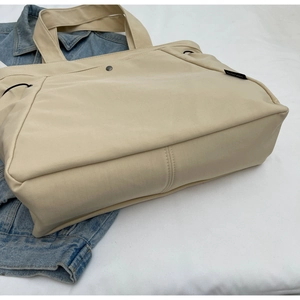 Detail of beige nylon tote bag featuring front snap pocket and durable woven handle