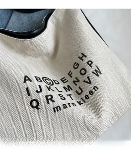 Close-up of herringbone canvas texture and black lettering on a large tote bag