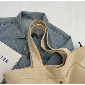 Detail of a beige nylon tote bag with dual stitching and a metal clasp on denim fabric