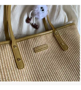 Détail d'un sac cabas en paille tissée avec anses en cuir jaune et breloque monstre en peluche