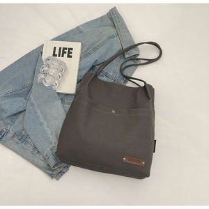 Close-up of a dark grey canvas tote bag with front pocket and leather logo detail