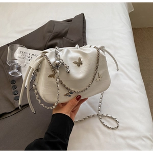 Détail du sac seau plissé blanc avec breloque papillon argentée et bandoulière chaîne