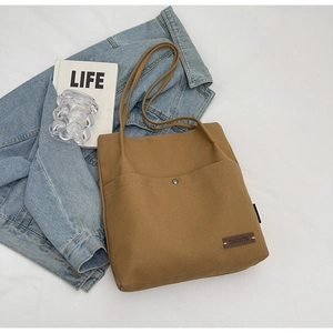 Detail of khaki canvas tote bag with front pocket, metal snap and branded leather patch