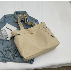 Detail view of large cream nylon tote bag with side drawstring and metal button closure