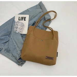 Top view of a large brown canvas tote bag with front pocket and shoulder straps on a table