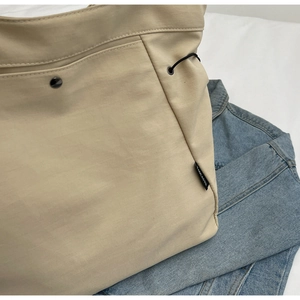 Macro view of beige nylon tote bag featuring black elastic drawstring and brand logo label
