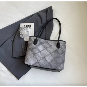 Detail of dark gray tote bag with quilted pattern and black leather trim on suit