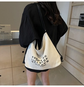 Detail of off-white canvas hobo bag featuring black letter print and adjustable strap