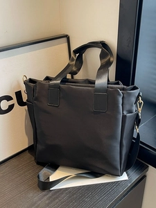 Minimalist black nylon tote bag with reinforced handles and adjustable shoulder strap