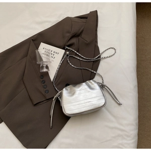 Détail de la bandoulière chaîne sur un sac seau plissé argenté porté sur une veste brune