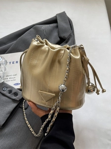 Metallic gold drawstring bucket bag with chain strap held against a grey suit jacket