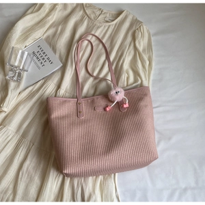 Détail d'un sac cabas en paille rose avec charm en peluche sur une robe plissée