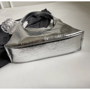 Detailed close-up of metallic silver hobo bag with pleated texture on white surface