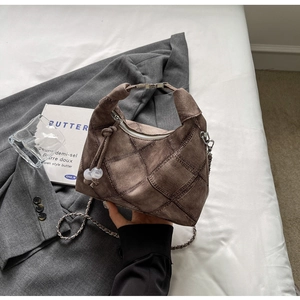 Detailed view of brown quilted handbag with silver chain strap and stylish ball charm