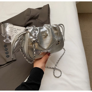 Détail d'un sac seau argenté avec papillons métalliques sur fond de blazer sombre