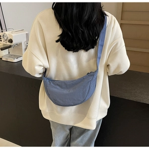 Model wearing a blue nylon crescent bag with wide shoulder strap in a cafe setting
