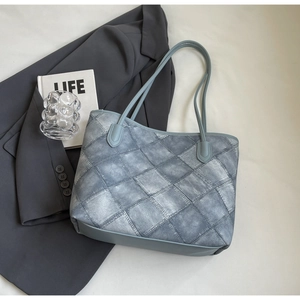 Detailed top view of large blue-grey tote bag with patchwork texture on blazer background