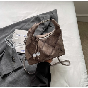 Detail of brown quilted suede handbag with decorative white beads and metal chain strap