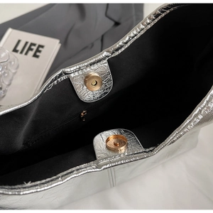 Detailed view of silver metallic bag featuring cracked texture, magnetic clasp and black lining