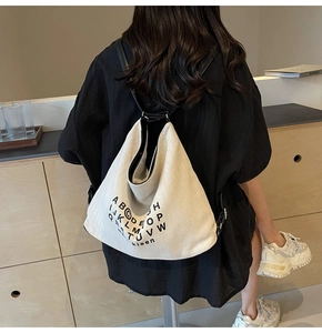 Rear view of a model wearing a beige canvas tote bag with black letter print and straps