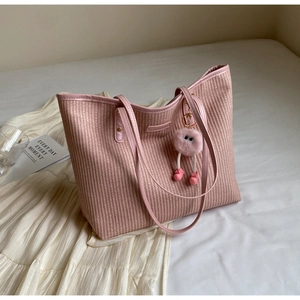 Grand sac cabas en paille rose avec anses en cuir et breloque peluche sur lit blanc