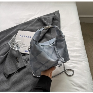 Blue quilted denim handbag with metal chain strap displayed on white bedding