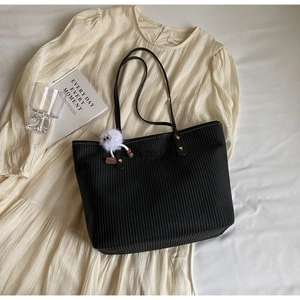 Détail du sac cabas en paille noire avec breloque en peluche sur une robe d'été