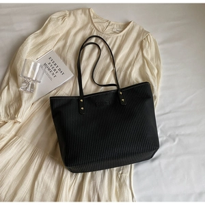 Détail du sac cabas noir texturé avec finitions dorées sur fond de robe blanche