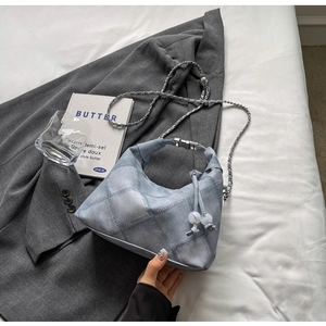 Detail of blue denim patchwork bag featuring chain strap and white bead drawstring closure