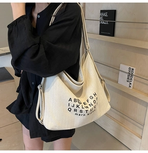 Detailed close-up of off-white canvas tote bag with black letter print and wide strap