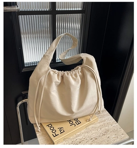 Dettaglio della borsa a spalla bianco sporco con coulisse e tracolla larga su pietra