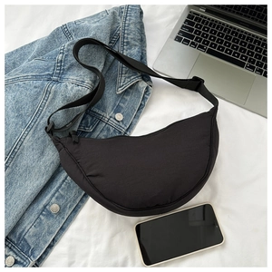 Close-up of black crescent dumpling bag in textured nylon with adjustable strap and laptop