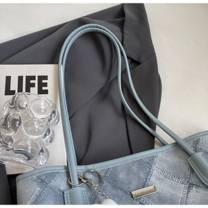 Close-up of light blue denim tote bag with metal logo plate and white fur ball pendant
