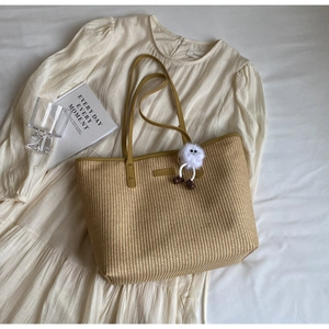Détail du sac cabas en paille avec anses en cuir jaune et breloque en peluche